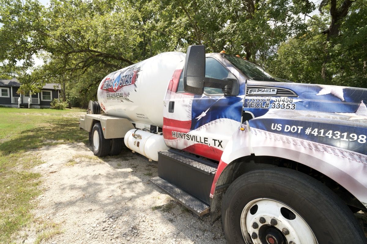 A Texas Star propane bobtail truck with American flag graphics and a Huntsville, TX address parked on gravel beside trees.