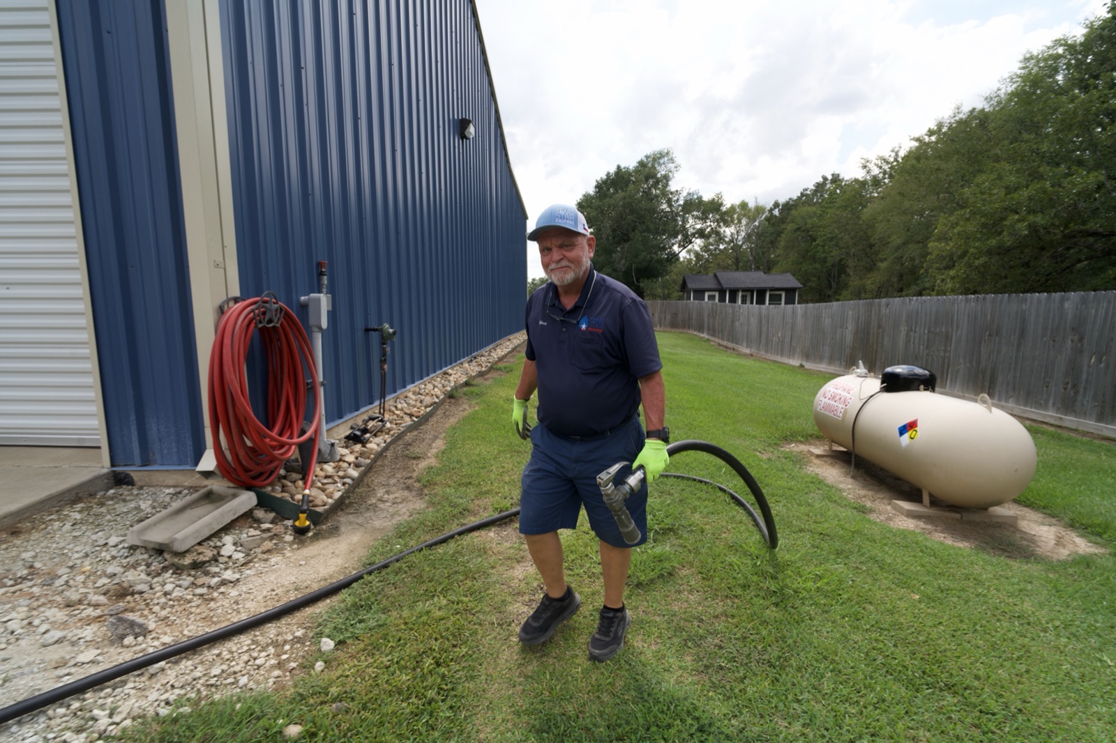 A Texas Star technician holding a delivery hose beside a propane tank.