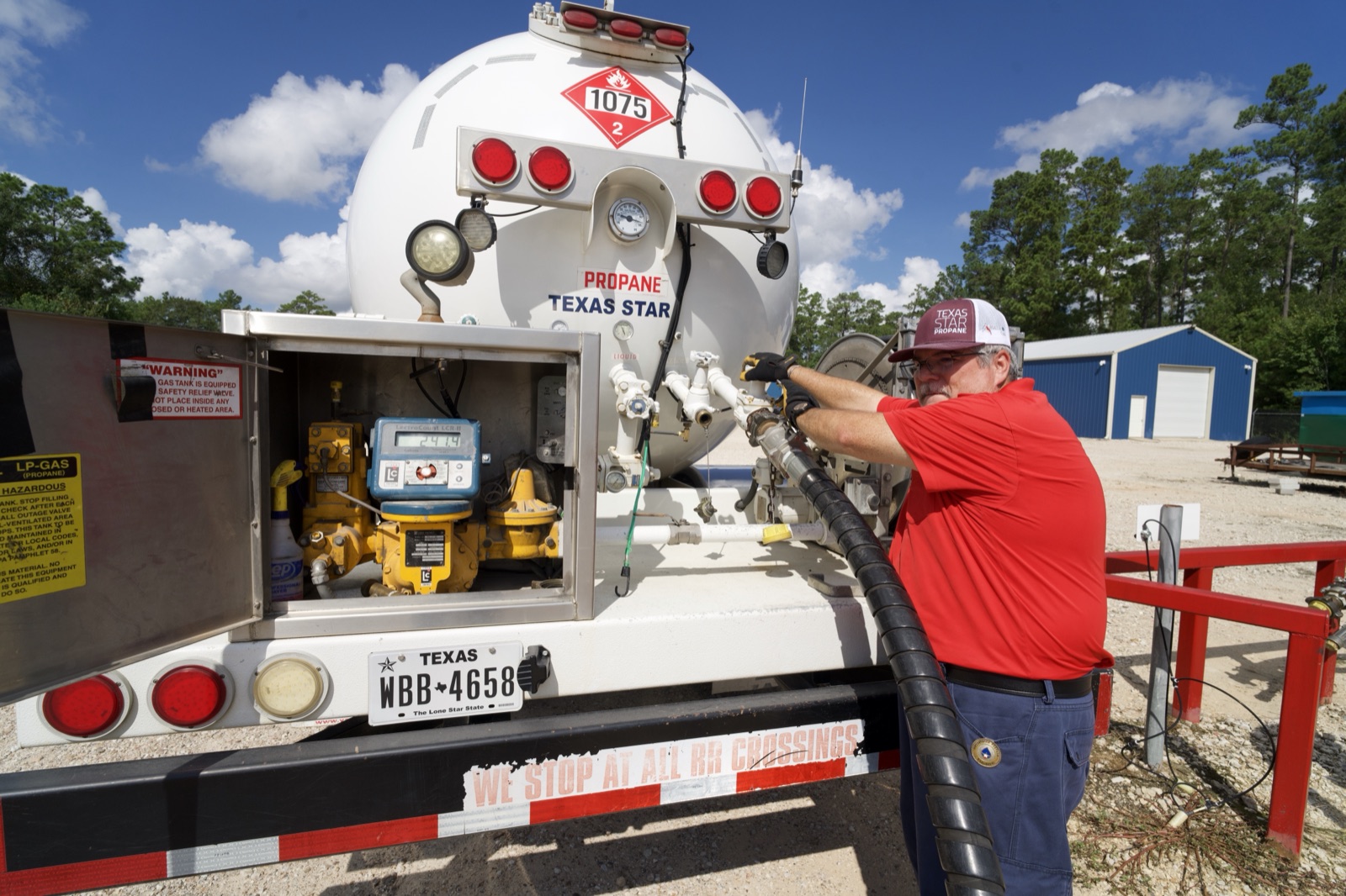 Driver operating the propane tank controls with visible branding and plate.