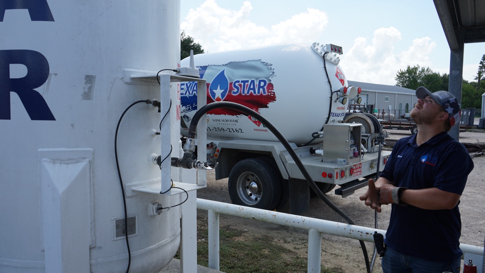 A Texas Star Propane technician fueling from a dispenser beside a storage tank.