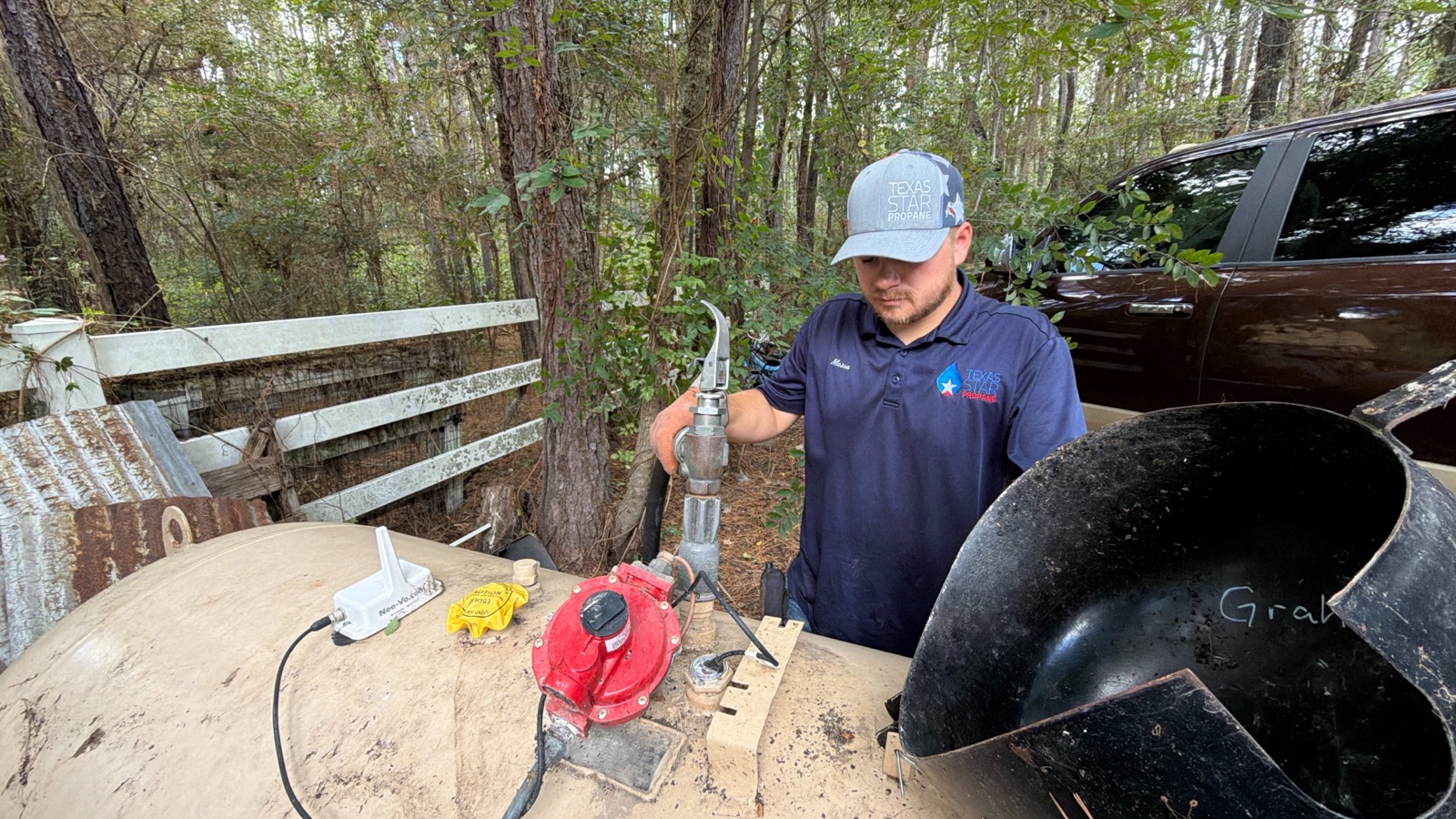 A technician servicing a propane tank with visible branding on his shirt.