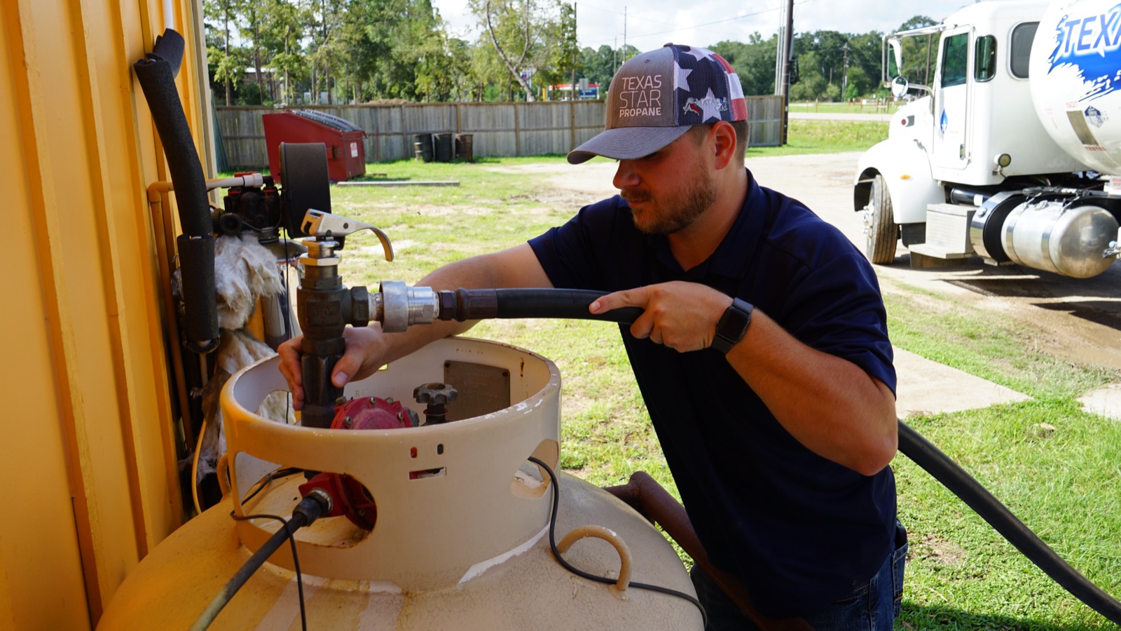A technician filling a propane tank with a branded truck behind.