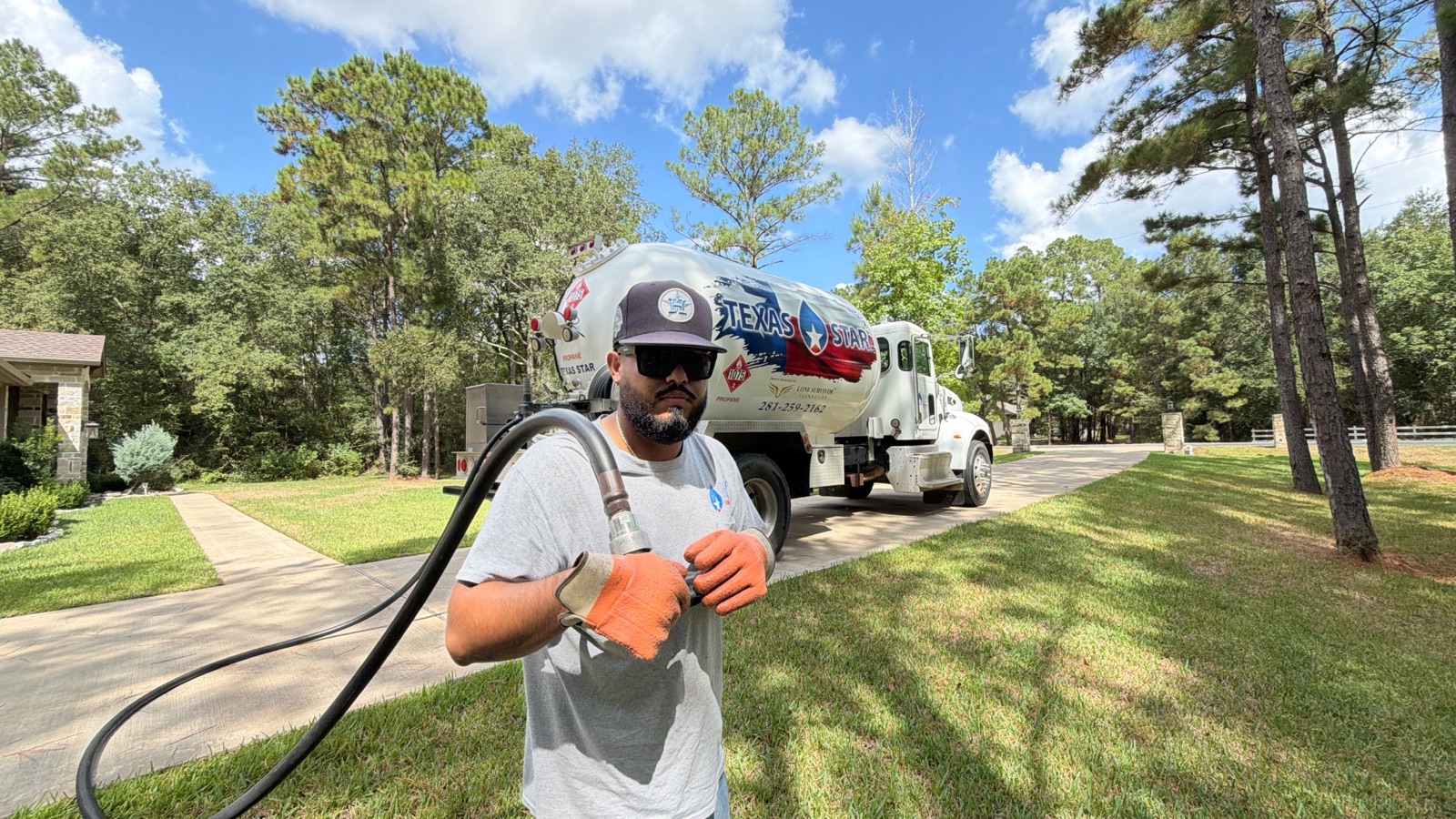 A driver with a delivery hose and branded tank truck in a residential driveway.