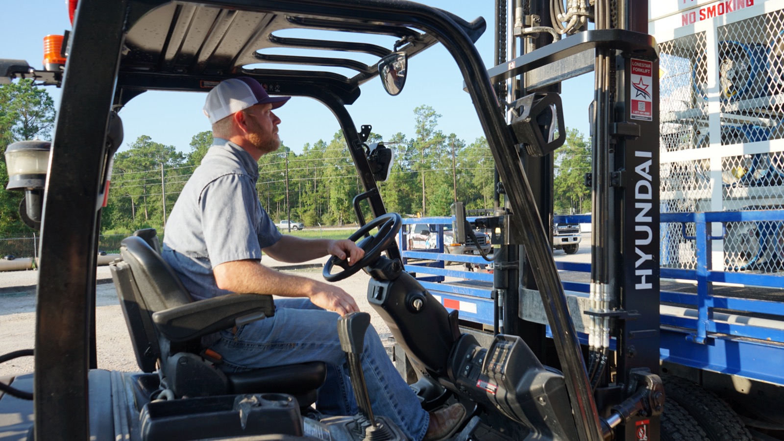 An operator at the controls of a propane forklift beside cylinder cages.