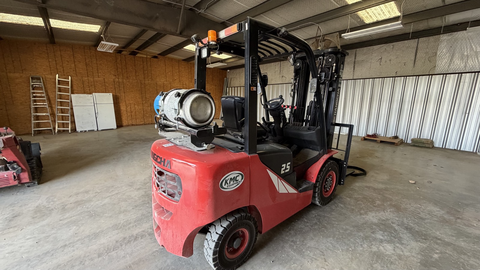 A propane powered forklift with its cylinder mounted, inside a warehouse.