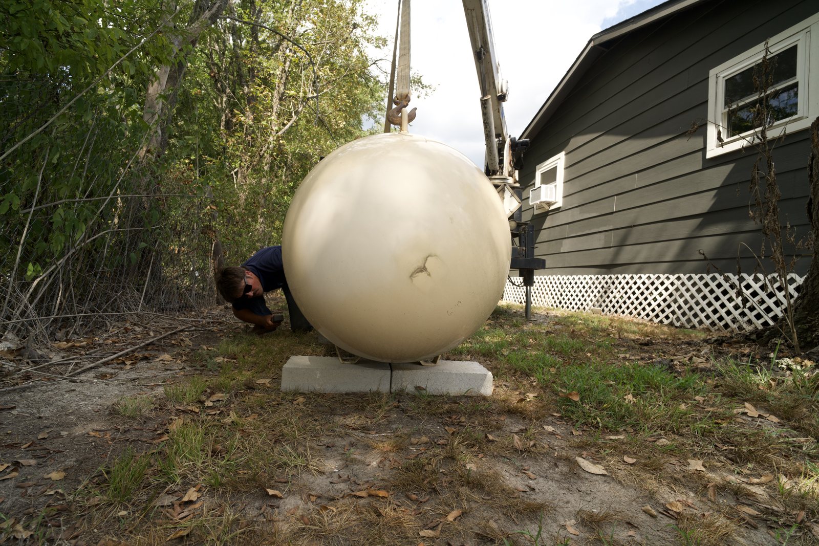 A propane tank being set on its pads beside a home by a boom truck.