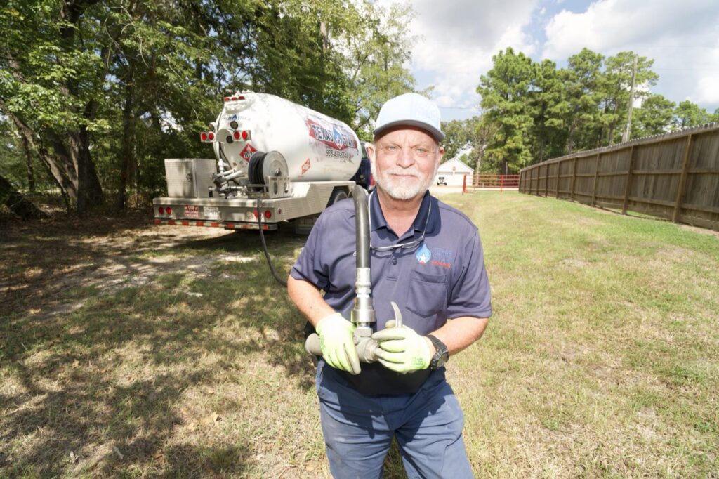 A Texas Star Propane driver pulling the delivery hose from a bobtail truck toward a residential propane tank