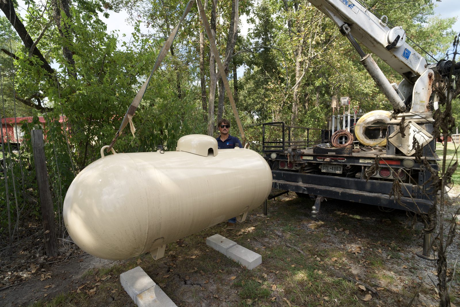 Bryan, TX technician installing a propane tank using a crane at a residential property