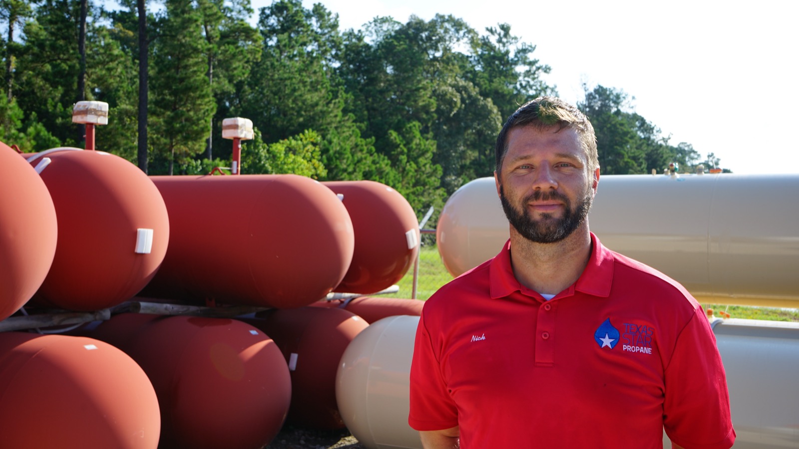 A Texas Star Propane team member in a branded shirt in front of bulk storage tanks.