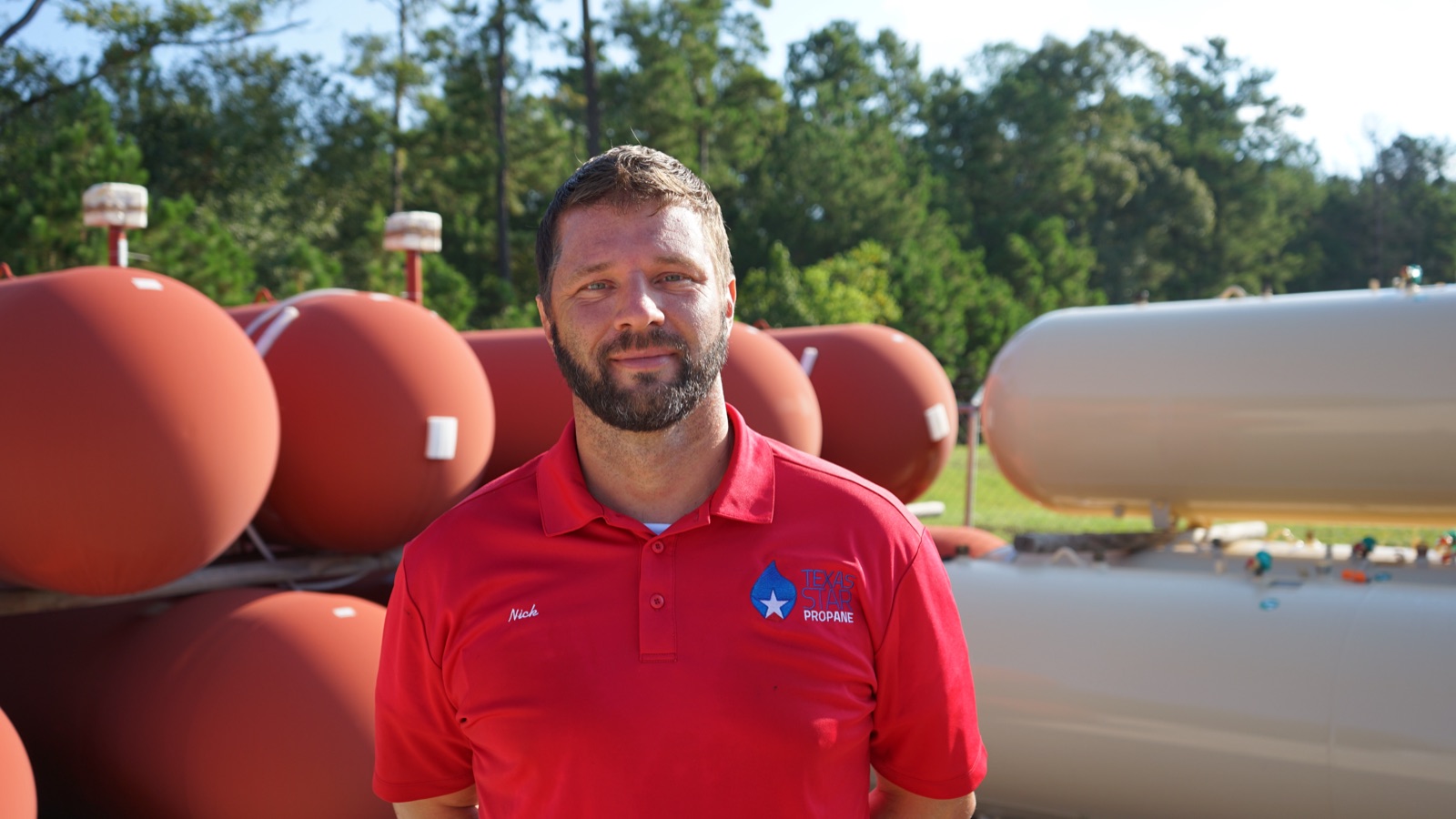 A Texas Star Propane employee in branded uniform with propane tanks behind