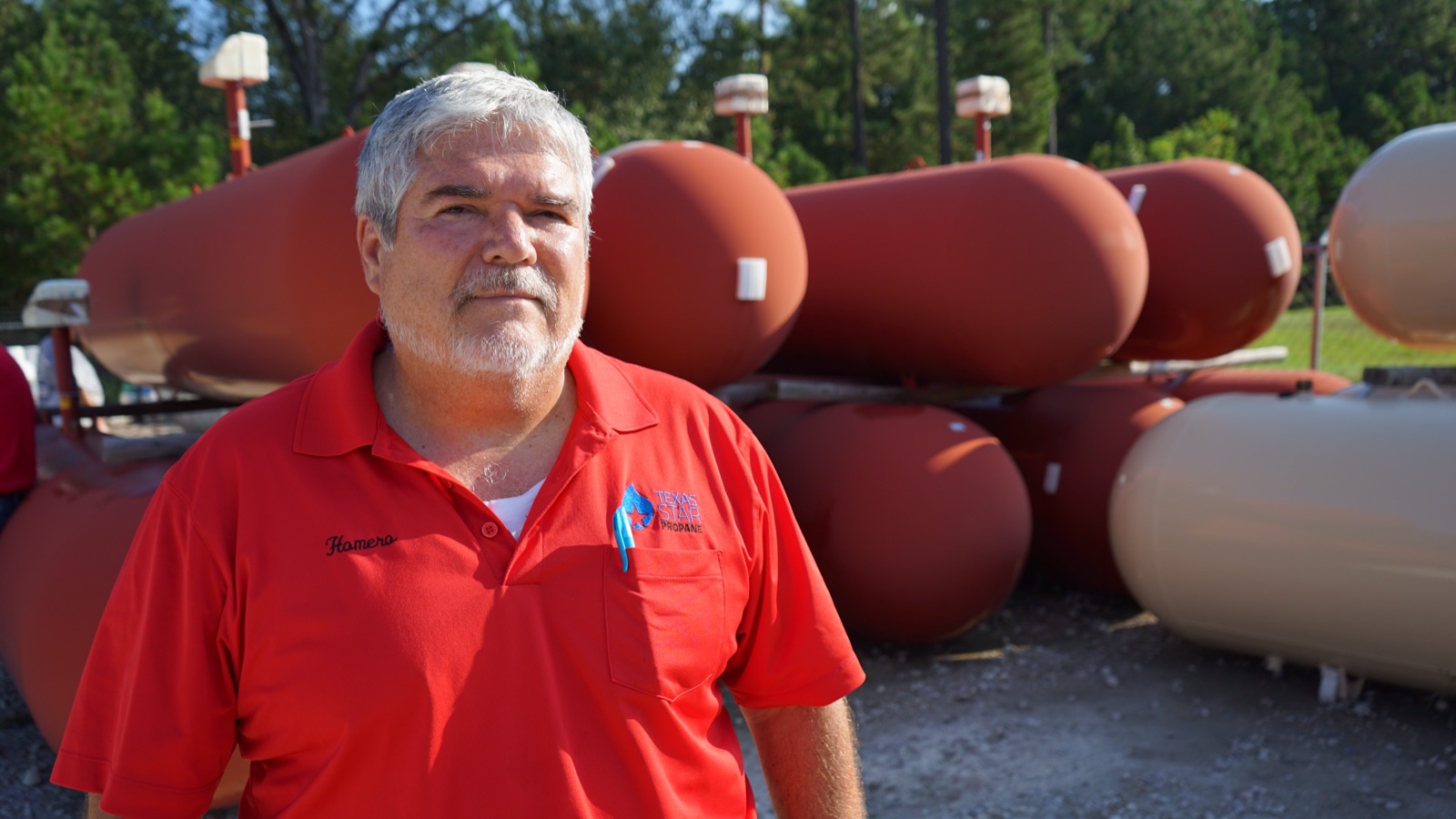 A Texas Star employee in a branded polo standing in front of propane tanks.