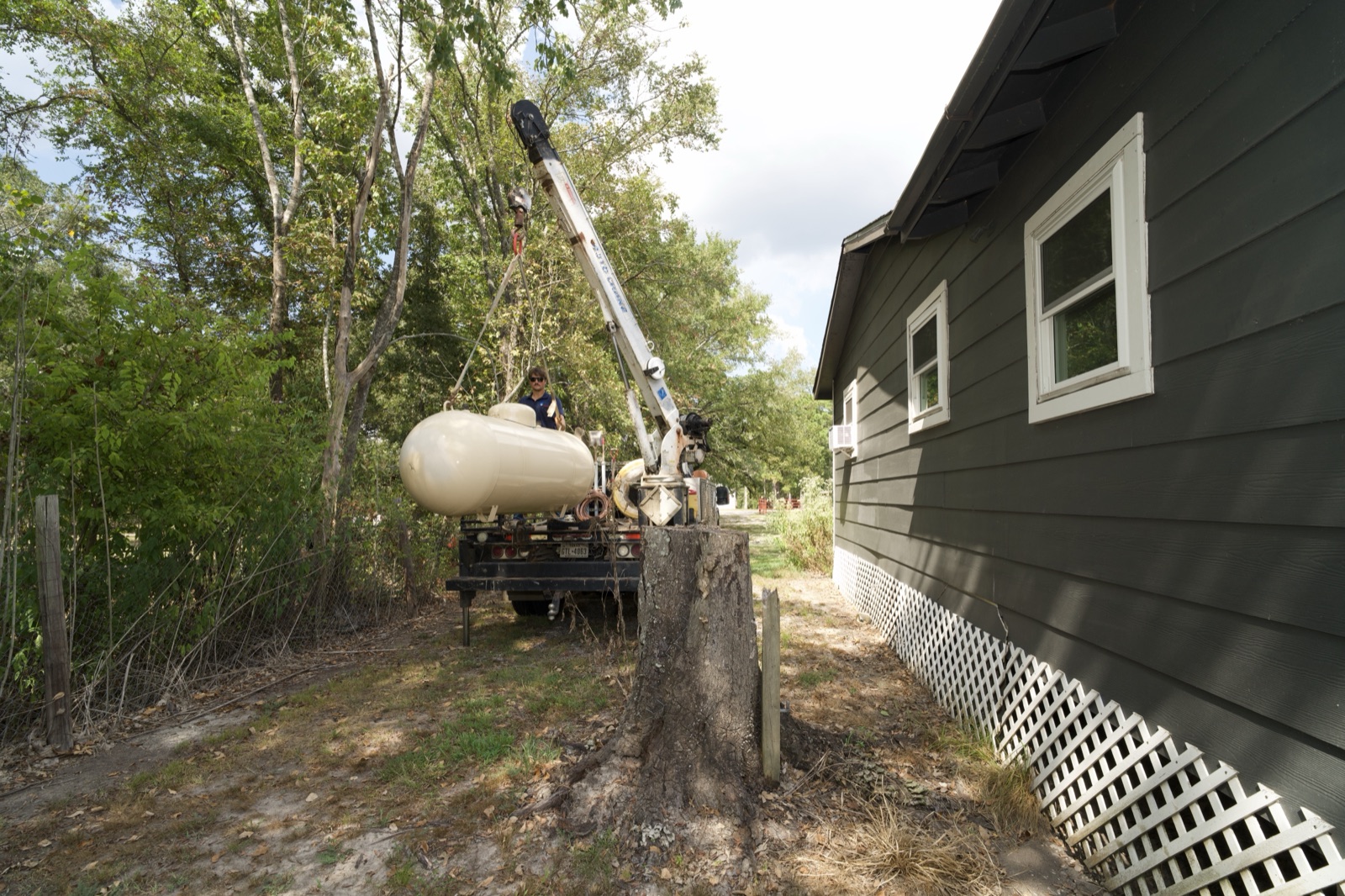 A propane tank being lifted by a boom truck beside a residence.